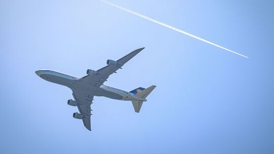 Ein Flugzeug fliegt unterhalb eines Kondensstreifens