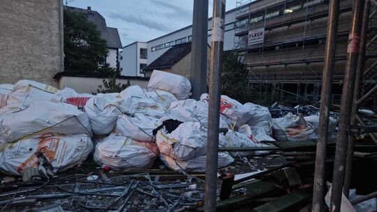 Mittlerweile steht ein Bauzaun um das ausgebaute Dämmmaterial, welches in Säcken lagert. Es handelt sich um KMF-haltige Dämmstof