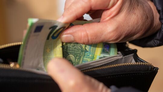 Eine Seniorin steckt Euro-Banknoten in eine Geldbörse