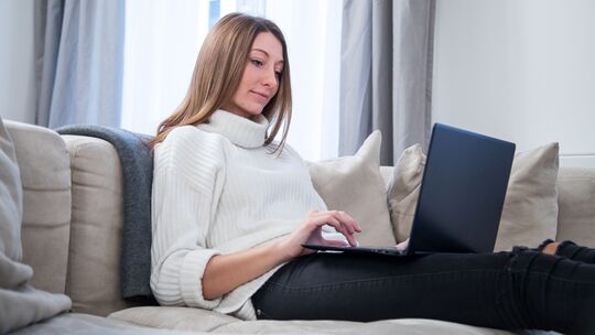 Eine Frau nutzt einen Laptop auf dem Sofa