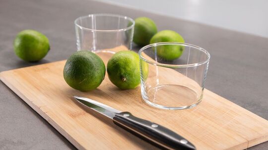 Limetten liegen neben zwei Schälchen auf einem Brett
