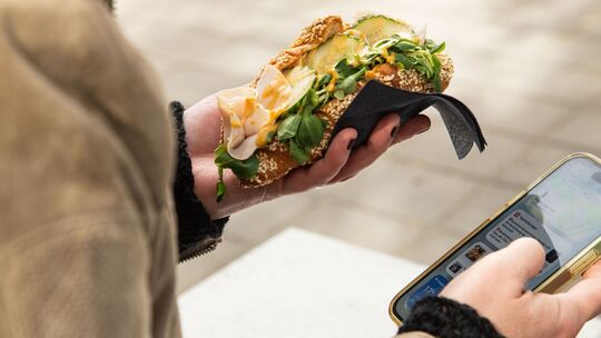 Eine Frau hält ein gefülltes Puten-Croissant und ihr Handy Eine Frau hält ein gefülltes Puten-Croissant und ihr Handy