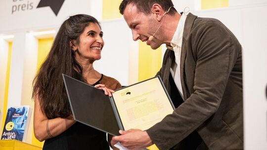 Die Gewinnerin des Deutschen Buchpreises 2026, Shida Bazyar erhält die Urkunde aus den Händen von Sebastian Guggolz, dem Vorsteh