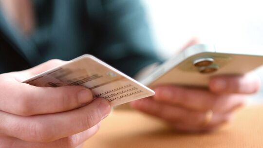 Eine Frau hält Personalausweis und Smartphone in den Händen