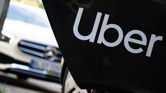 Ein Mietwagen mit einem Schriftzug des Mobilitätsdienstleisters und Fahrtenvermittlers Uber steht vor einem Taxi, das auch über