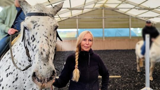 Tiertherapeutin Jutta Mengel führt eines der Therapiepferde mit Reiter durch die Halle.