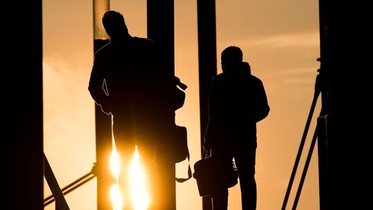 Zwei Männer gehen mit Aktentasche bei Sonnenaufgang über Brücke Zwei Männer gehen mit Aktentasche bei Sonnenaufgang über Brücke